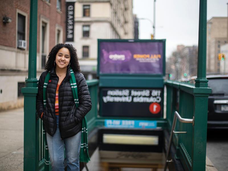 A young woman stands in front of the train entrance.