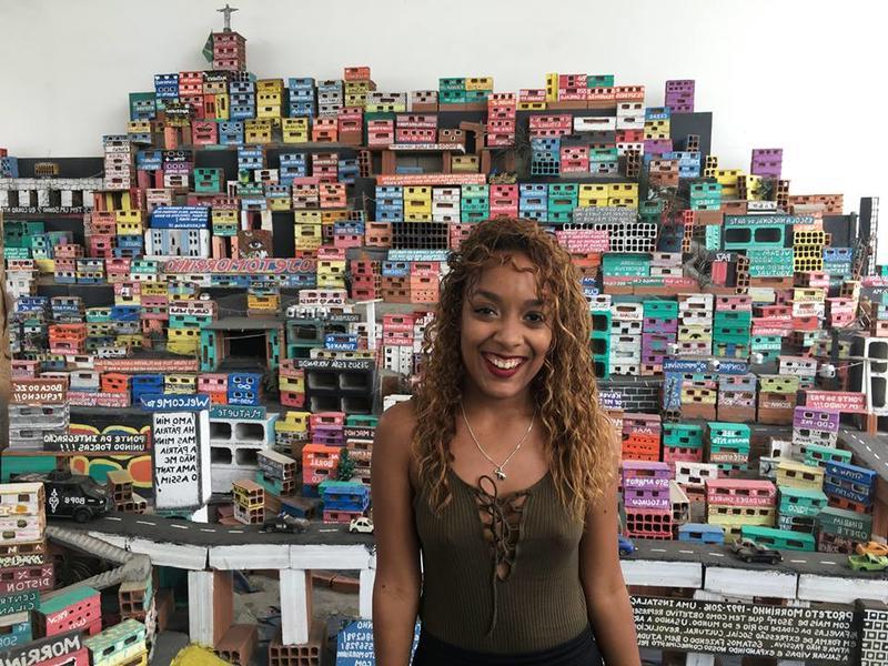 Brown-skinned woman in Rio with colorful models of buildings behind her